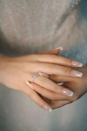 Close-up of bridal manicure and diamond engagement ring on elegant hands.