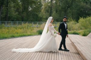 Bride and groom walking on wooden deck with scenic nature background.