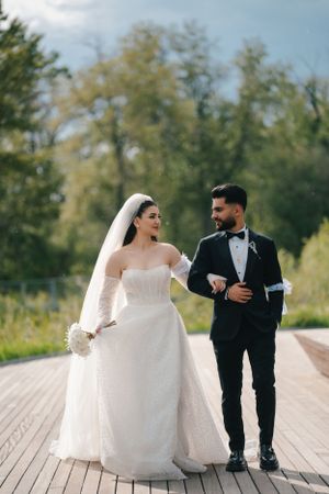Happy newlyweds walking together on wooden boardwalk surrounded by greenery.