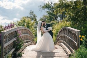 Wedding couple embracing on a rustic wooden bridge surrounded by lush greenery on their special day.