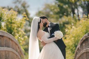 Romantic wedding moment captured on wooden bridge with white bouquet and long flowing veil.