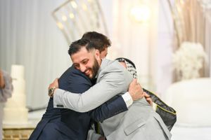 Two men in formal attire share an emotional embrace during a wedding celebration.