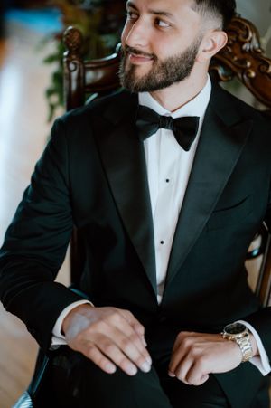 A close-up portrait of a groom in classic black tuxedo and bow tie.