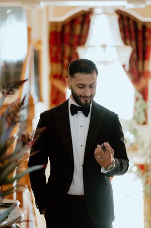 Indoor portrait of a groom in classic tuxedo against elegant interior with red curtains.