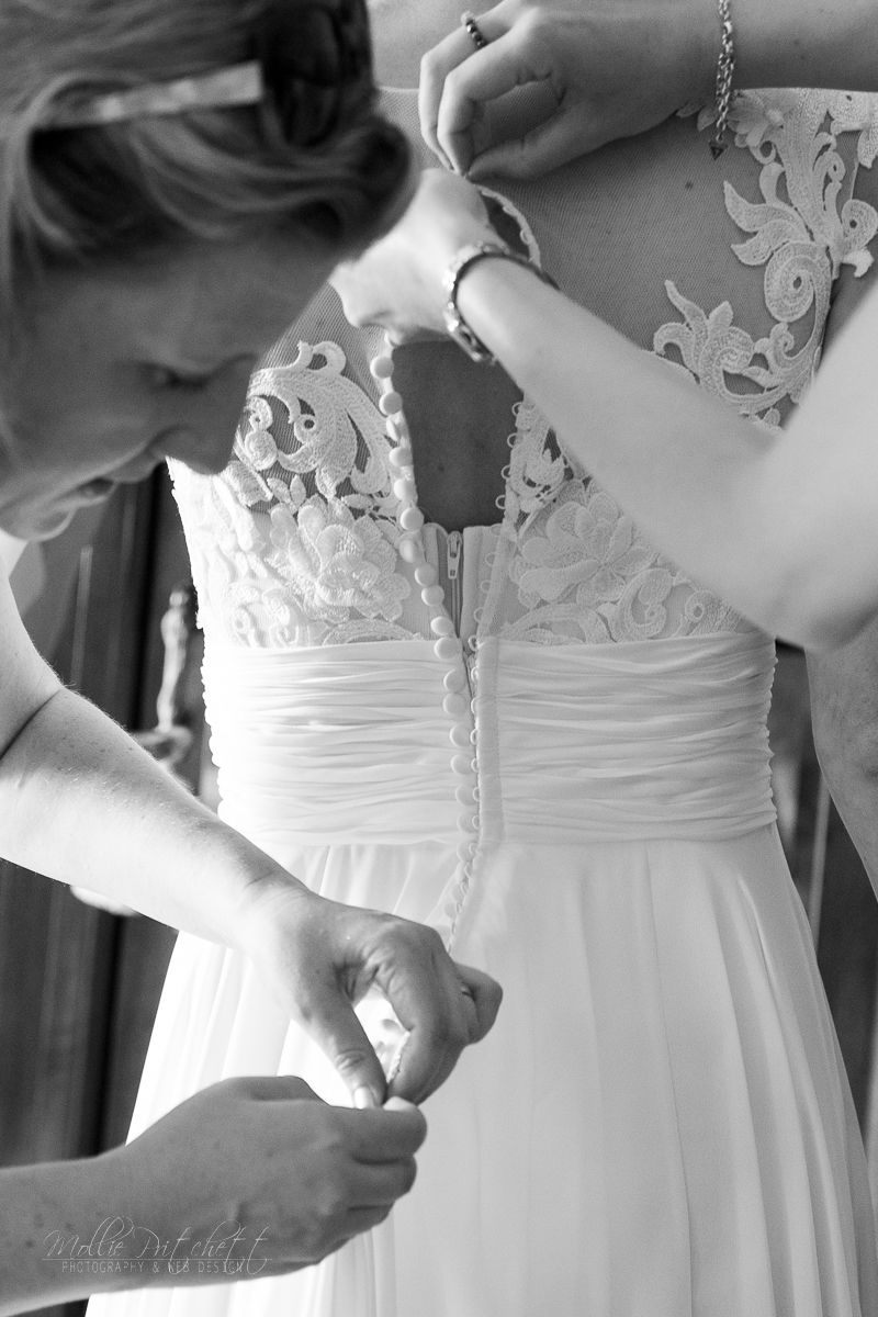 Black and white detail shot of hands buttoning an intricate lace wedding dress.