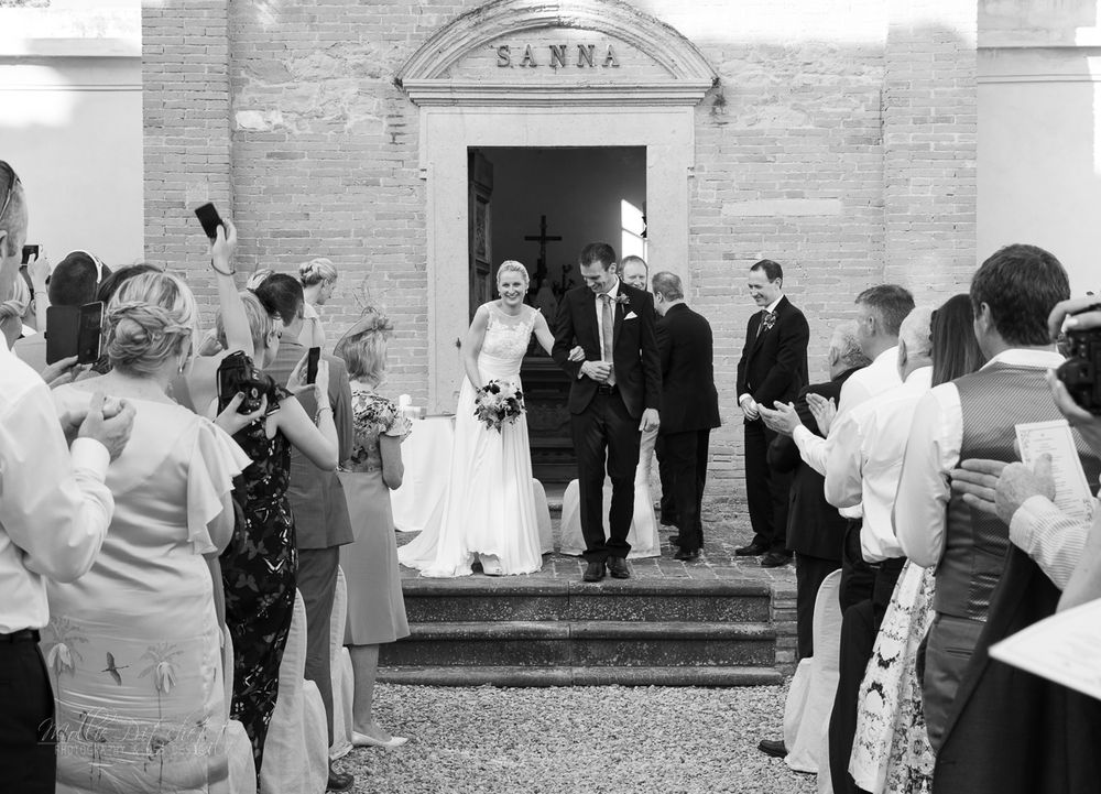 Black and white photo of newlyweds exiting a church while guests throw confetti.