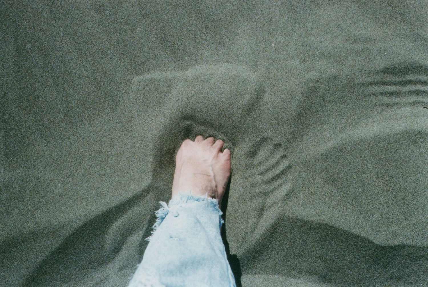 A bare foot steps into shallow water creating ripples on a sandy surface.