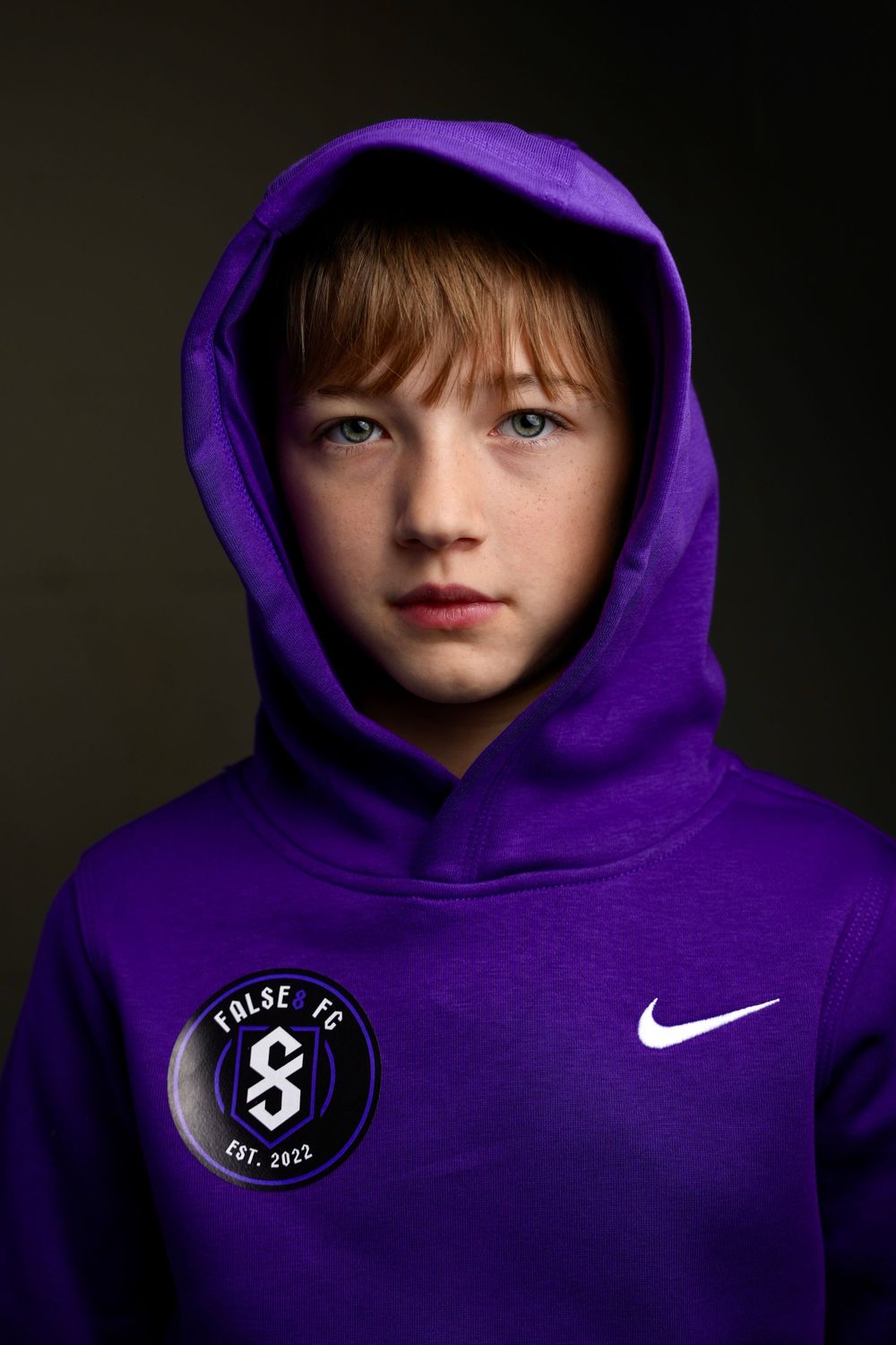 Portrait of a youth wearing a purple Nike hoodie with a circular patch against a dark background.