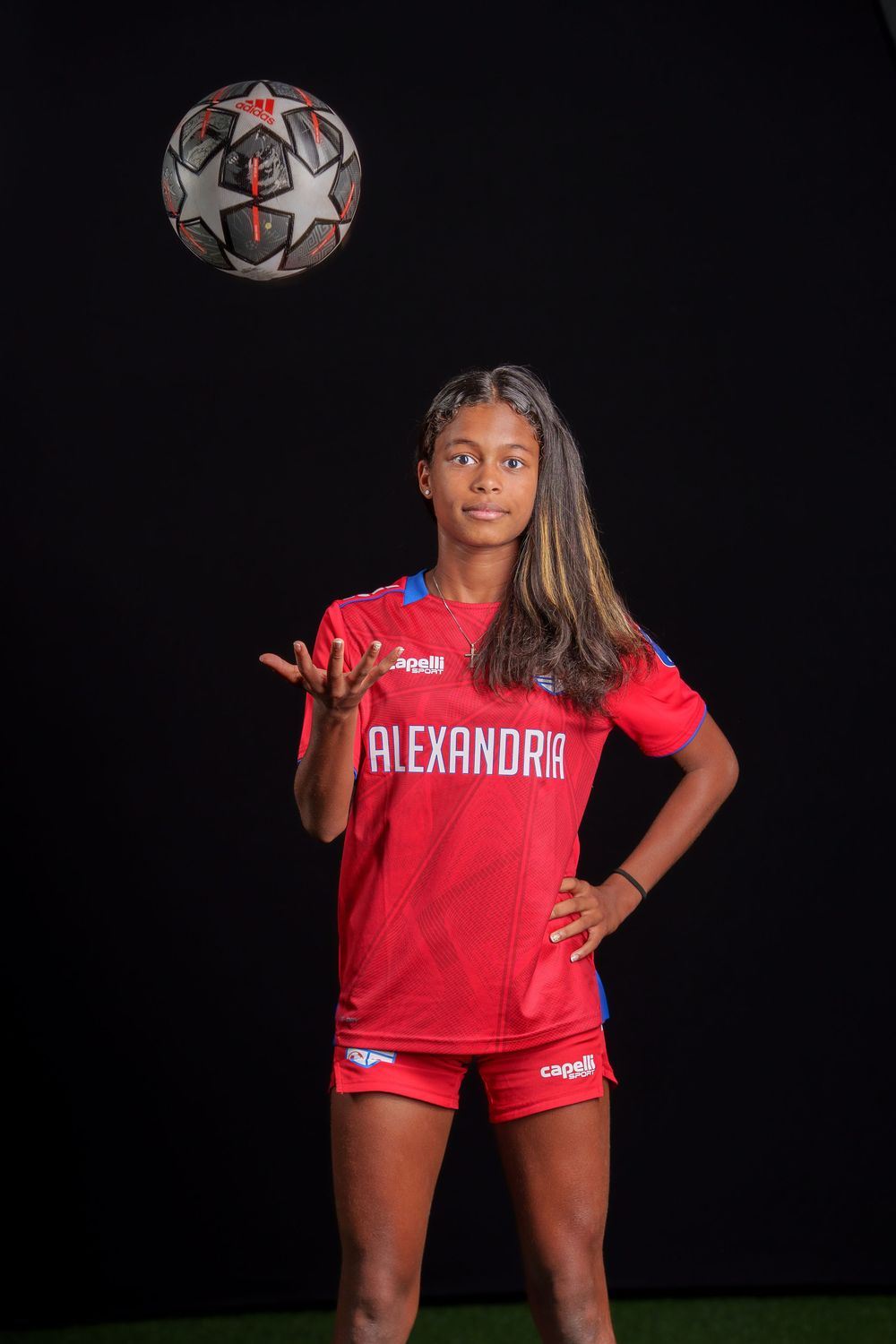 Soccer player in red Alexandria jersey poses with ball against dark background for athletic portraits.
