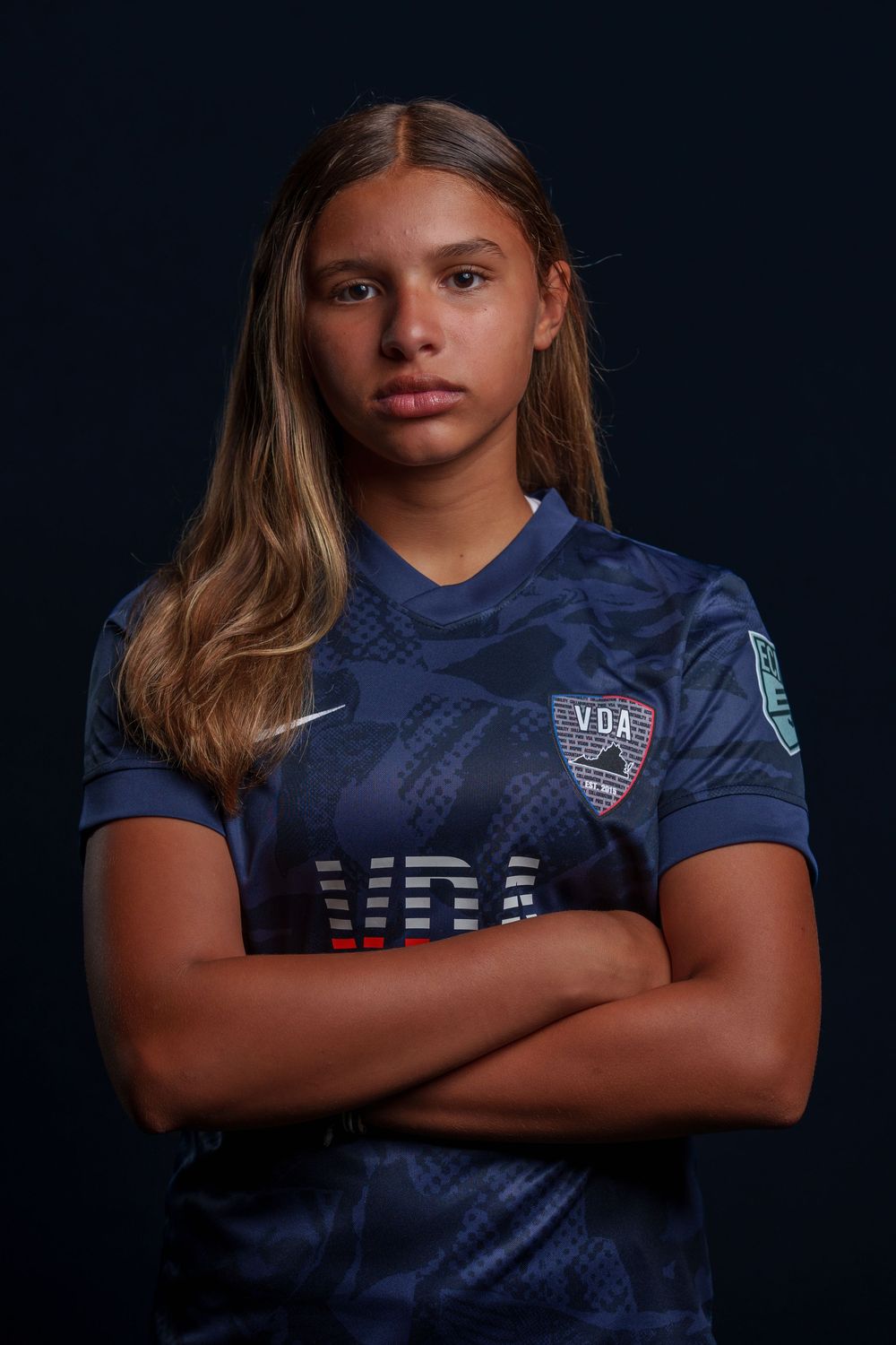 Professional soccer player poses in dark blue USA team jersey against black background.