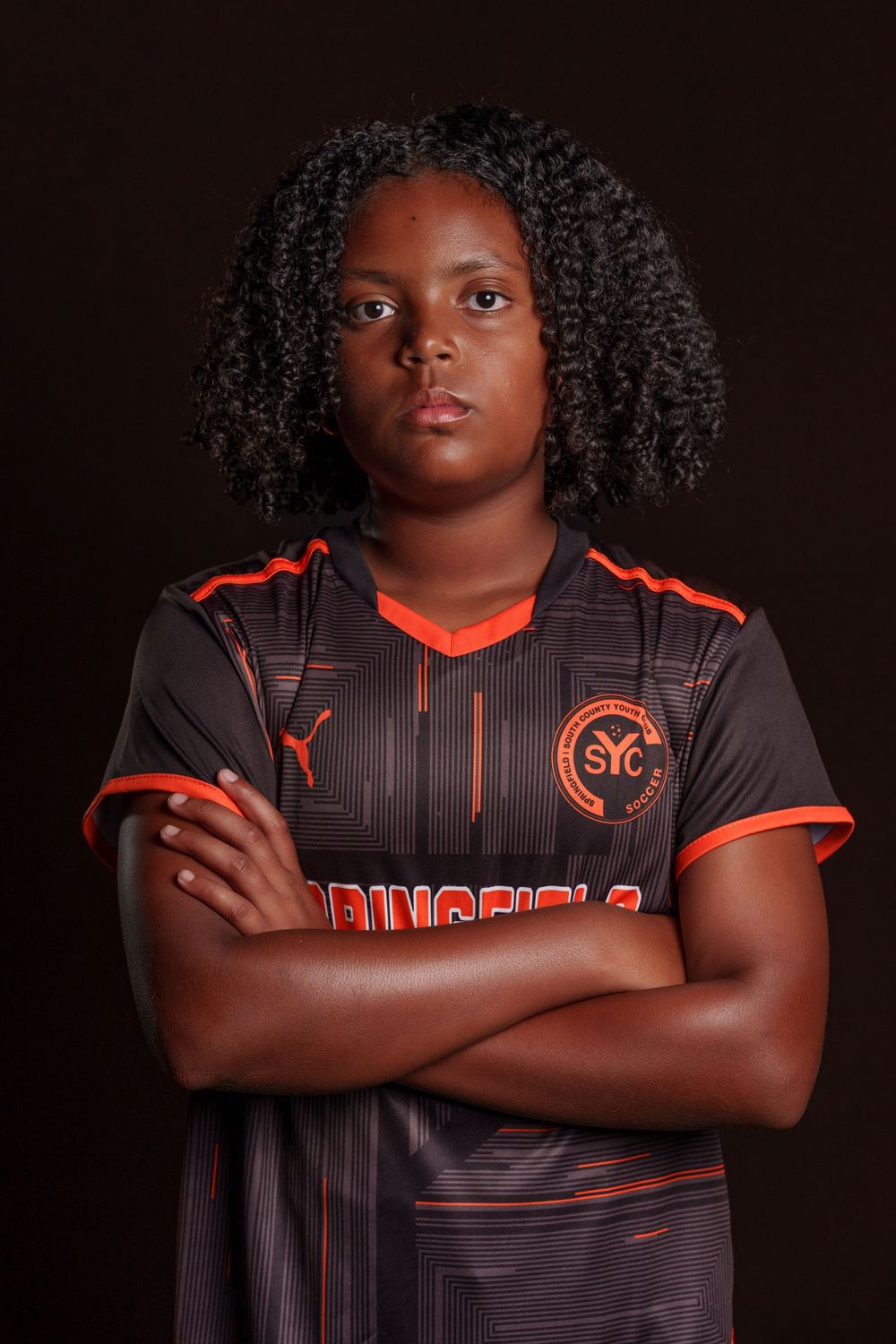 Athlete in black and orange striped sports uniform poses against dark background for dramatic team photo shoot.