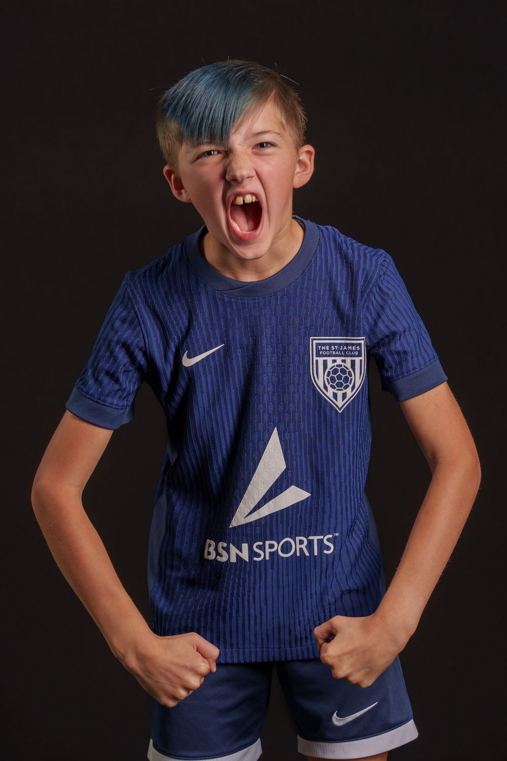 Young athlete in blue BSN Sports soccer uniform showing intense emotion against dark background.