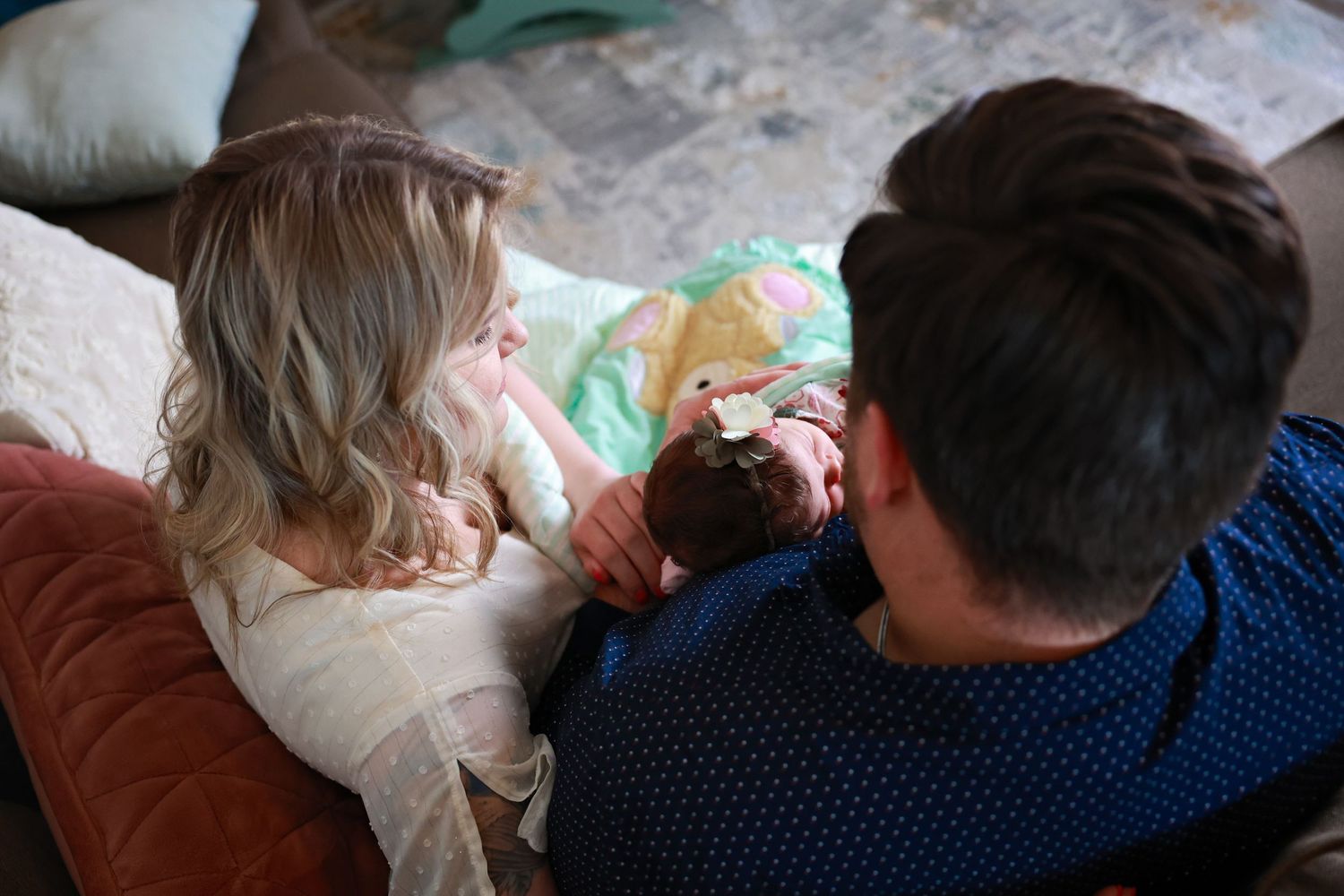 Two people sit closely together on a couch while looking down at newborn in home new session Carlsbad, Roswell, Hobbs NM