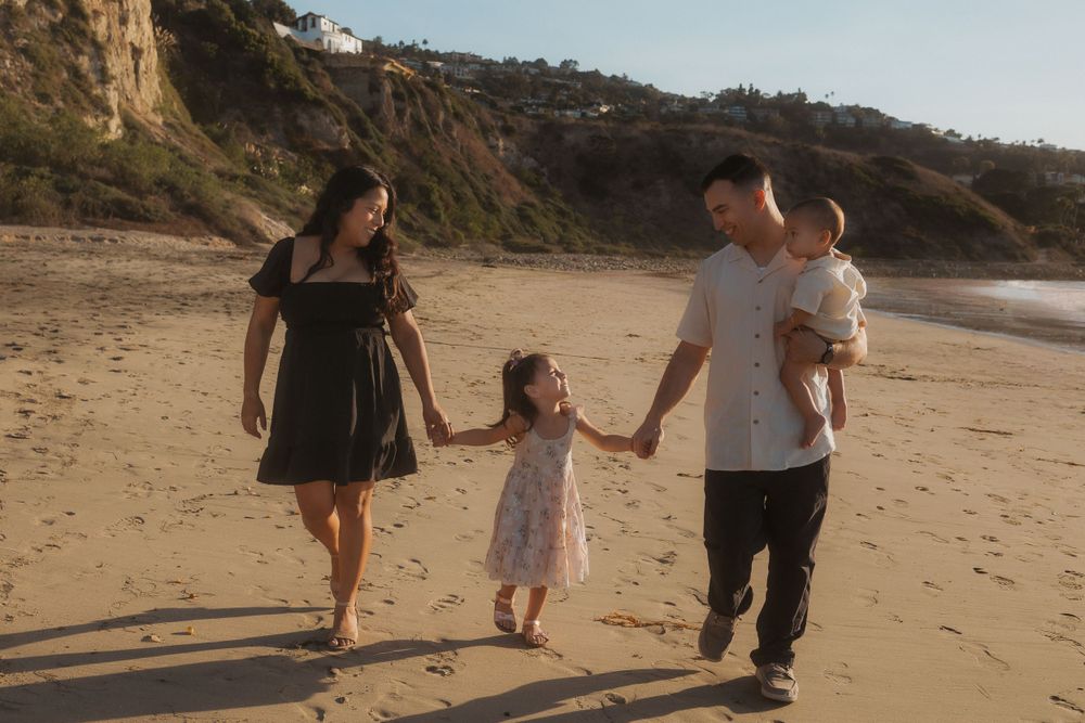 Family of four walking together on sandy beach with coastal cliffs in background.