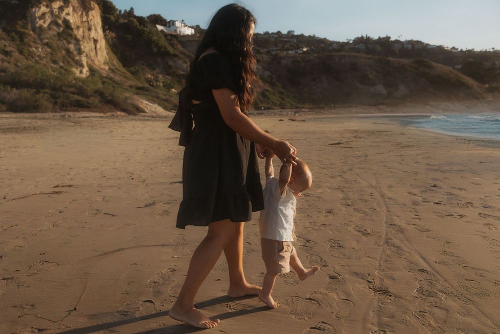 Parent and child walk hand in hand along scenic beach at golden hour.