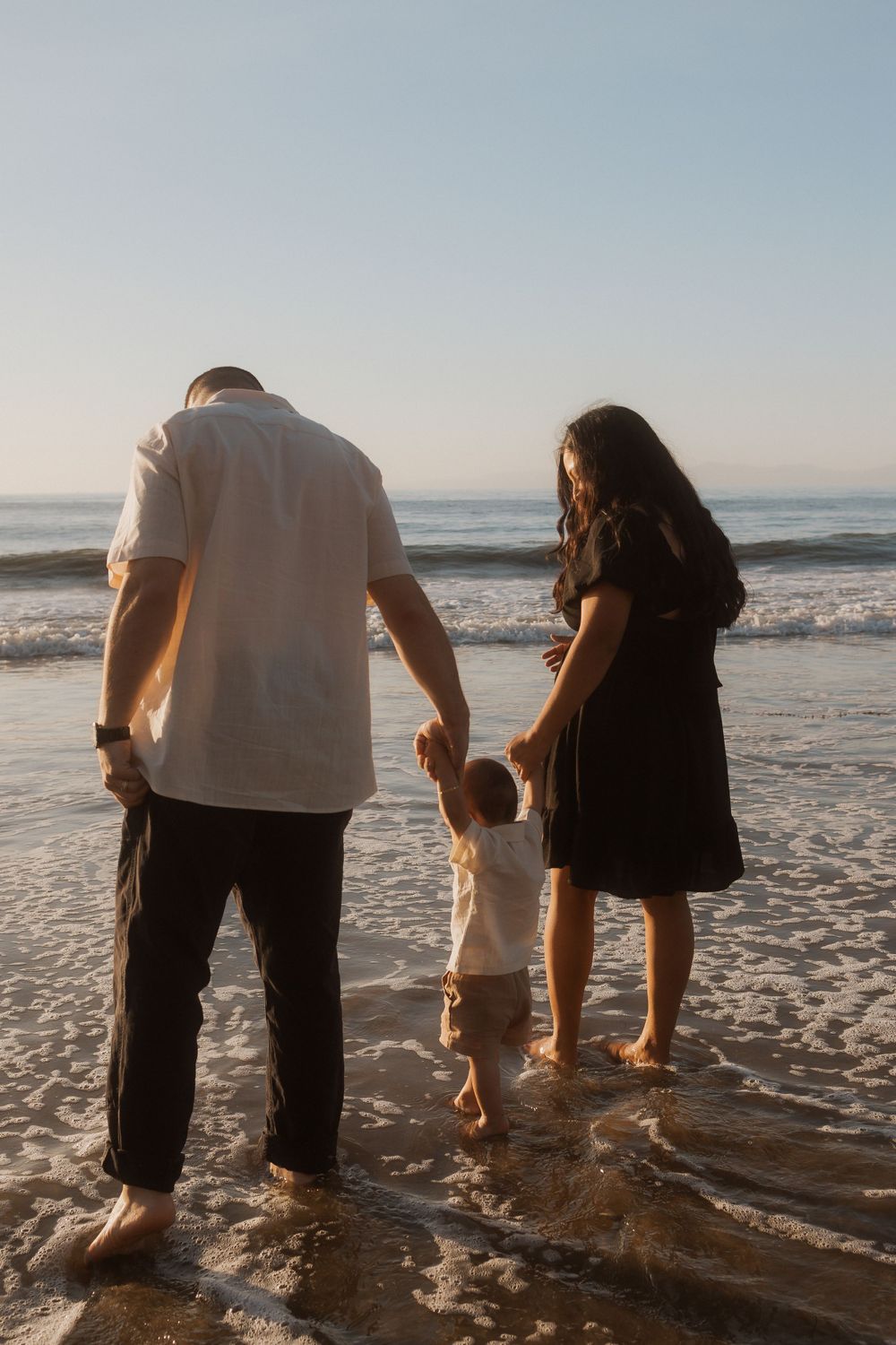 A couple holding hands with a small child at the beach during golden hour.