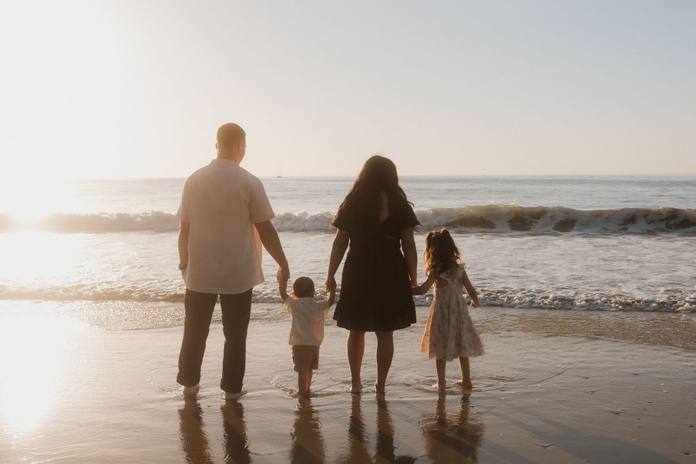 A family of four walking together on a sunset beach with waves in the background.