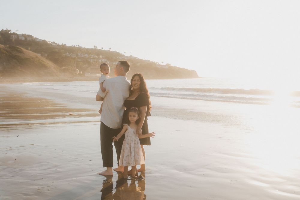 A family stands together watching the ocean waves on a misty beach.