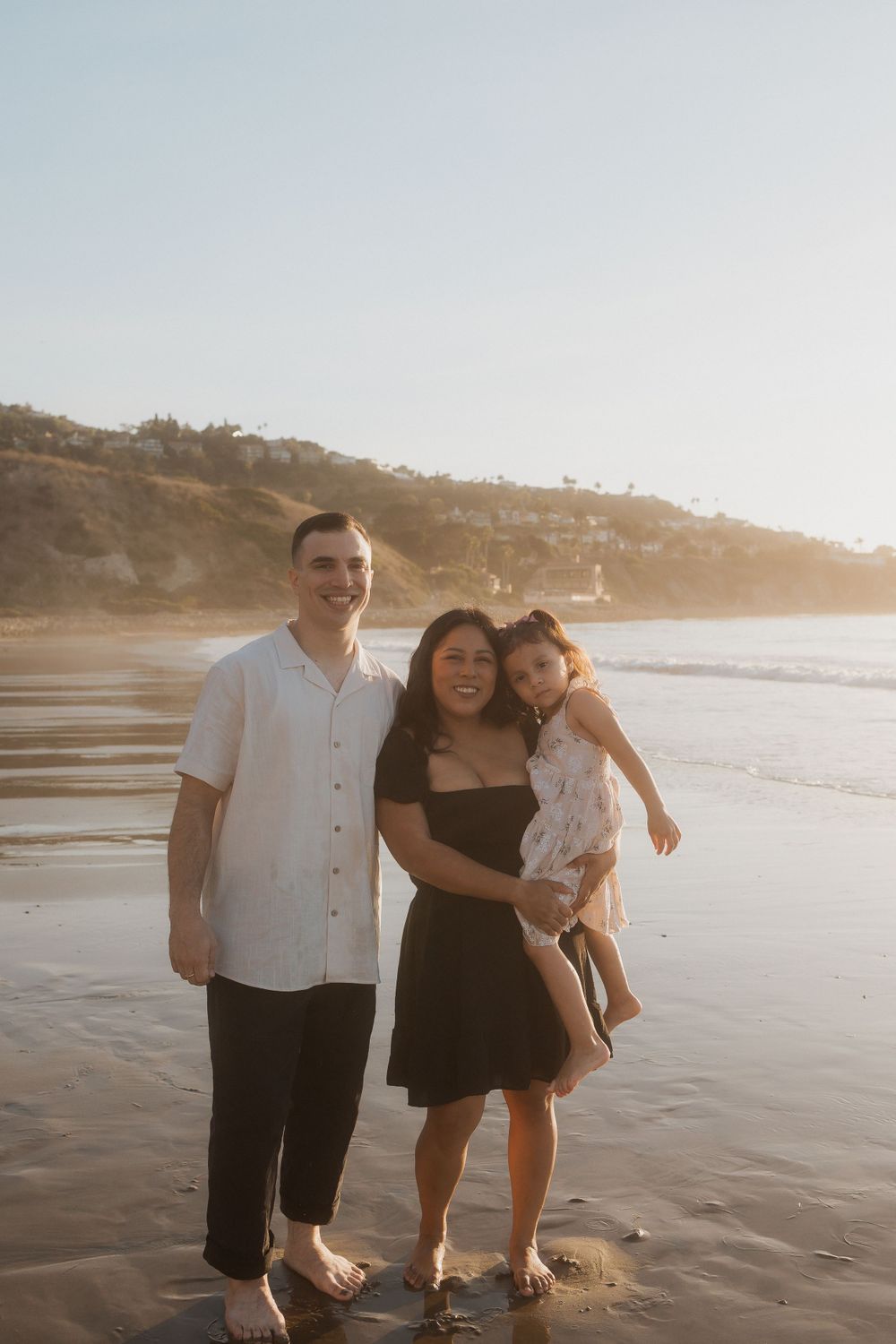 A happy family enjoying a sunset beach photoshoot against coastal cliffs.