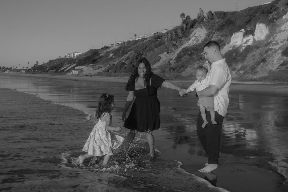 A black and white photo of a family playing in the ocean waves near coastal cliffs.