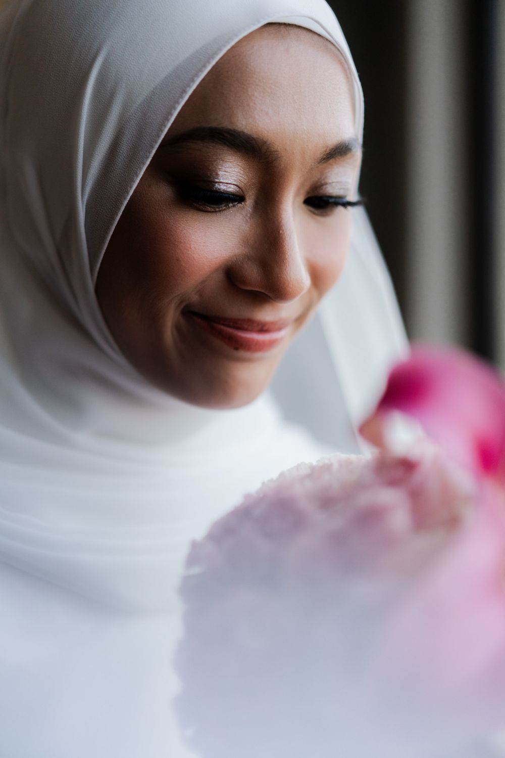 A close-up portrait of a bride in white hijab with subtle makeup and a gentle smile.