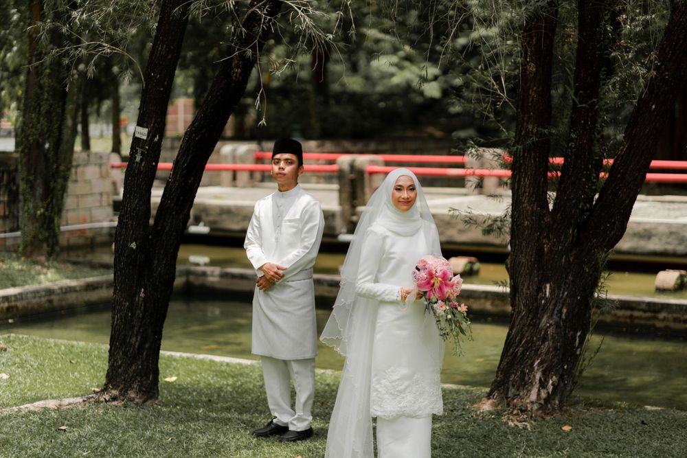 A bride and groom in traditional Muslim attire pose in a park setting.