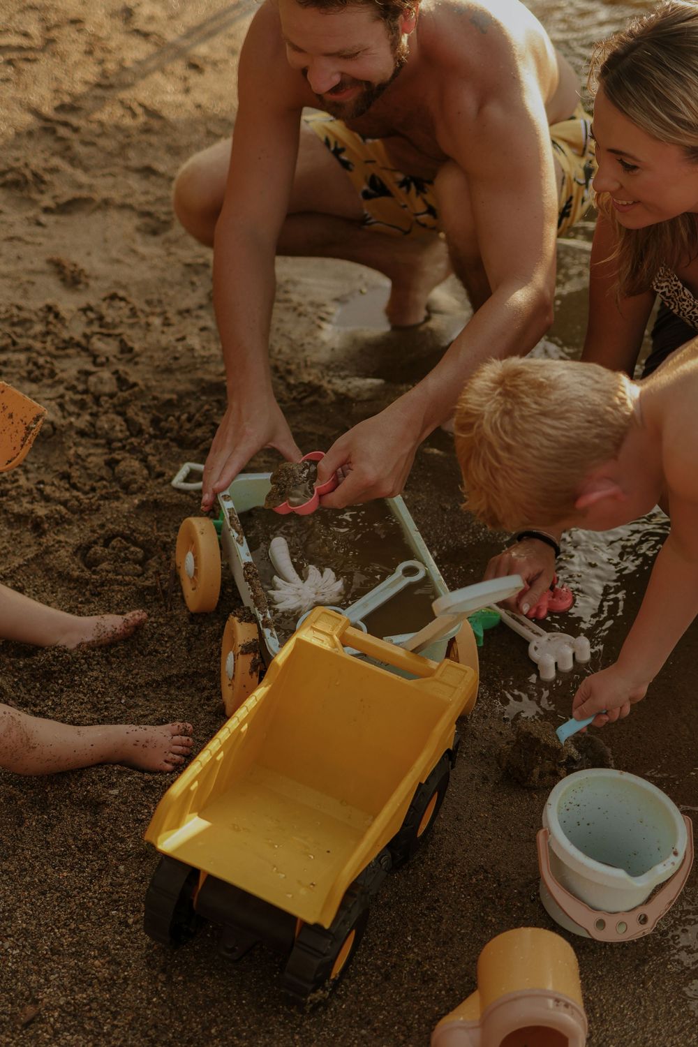 Family playing with toys in the sand at the beach during sunset.