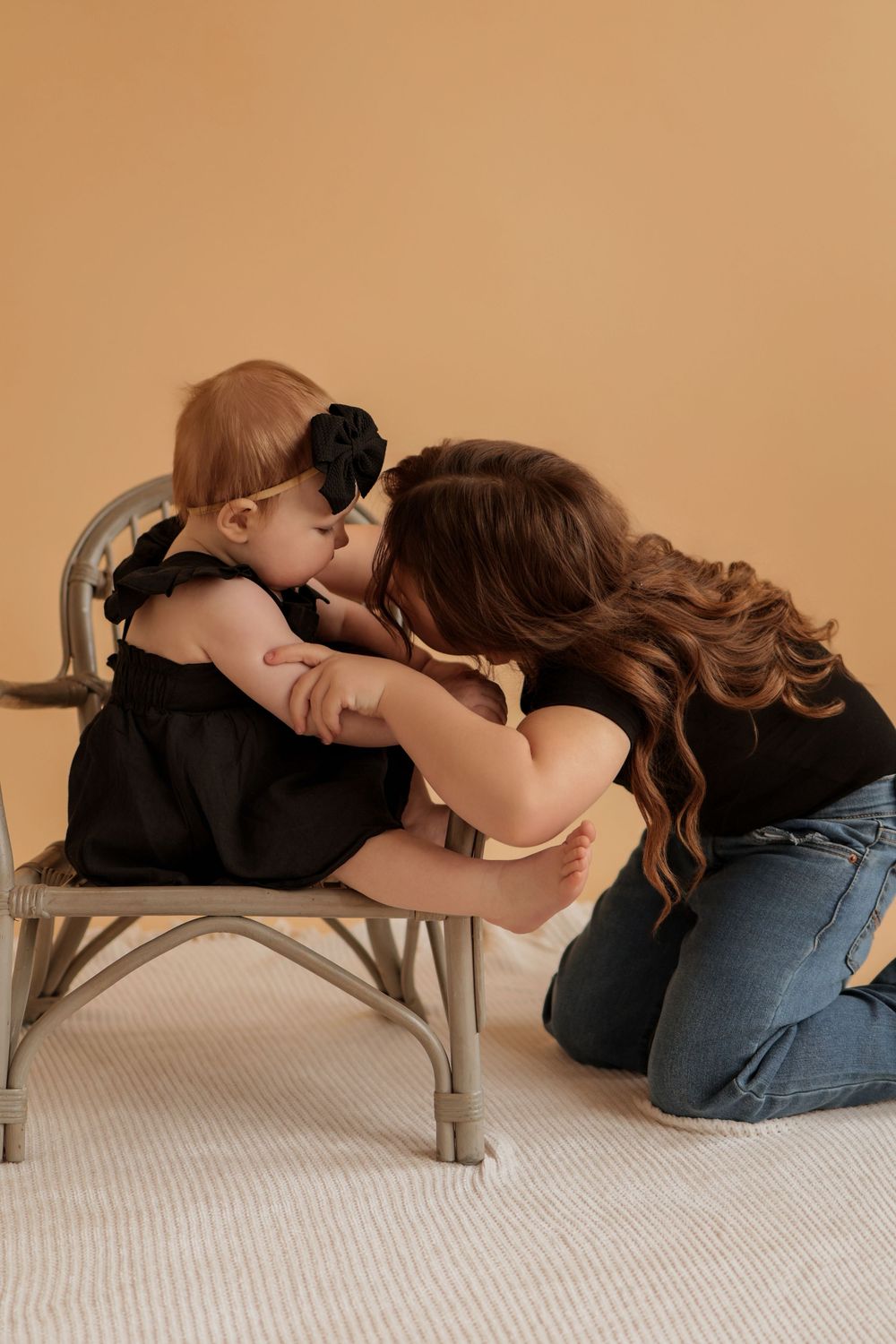 Mother and baby sharing tender moment on wooden chair in studio setting.