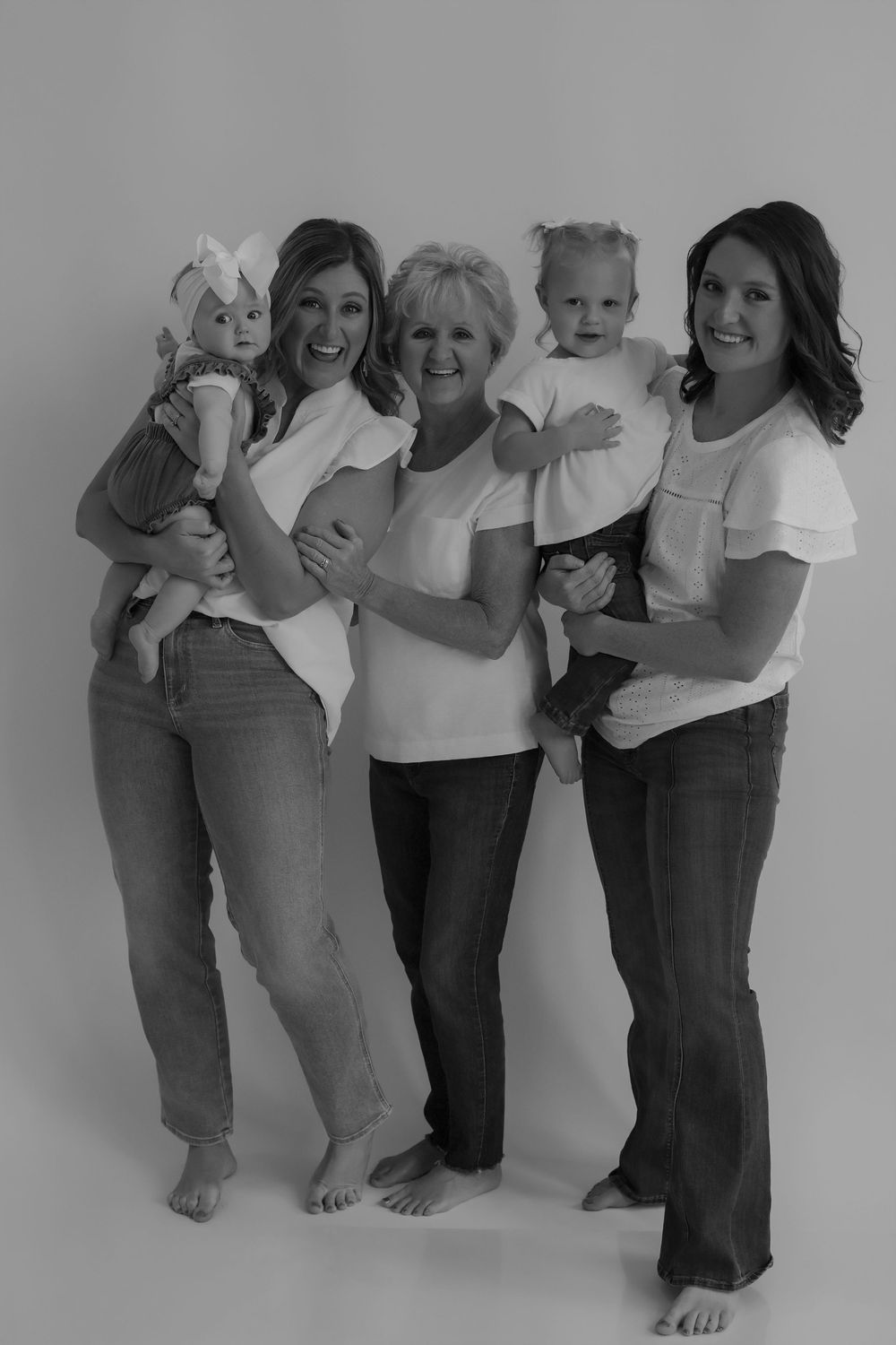 Multi-generational family portrait in coordinated white outfits against grey background.