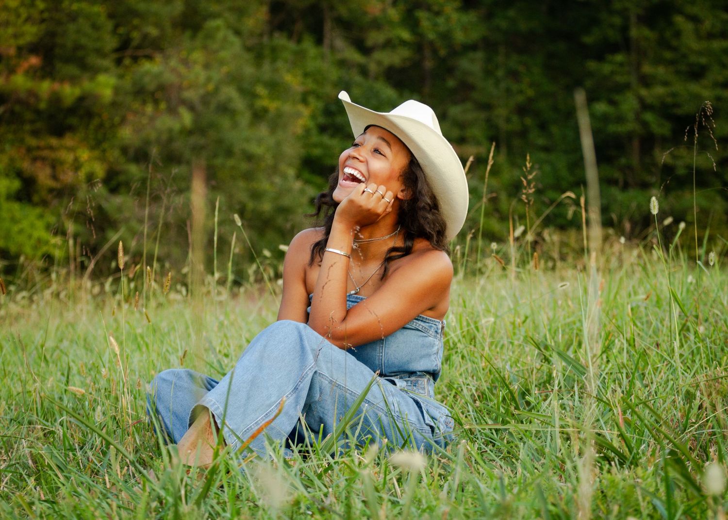 Girl in cowboy hat sitting in a grassy green field