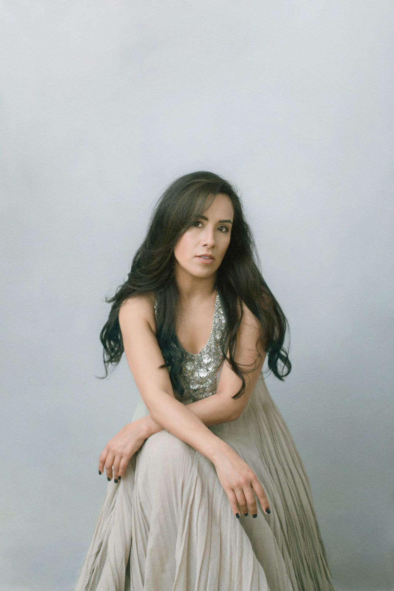 A person in a silver sequined top and flowy beige skirt poses elegantly against a gray backdrop.