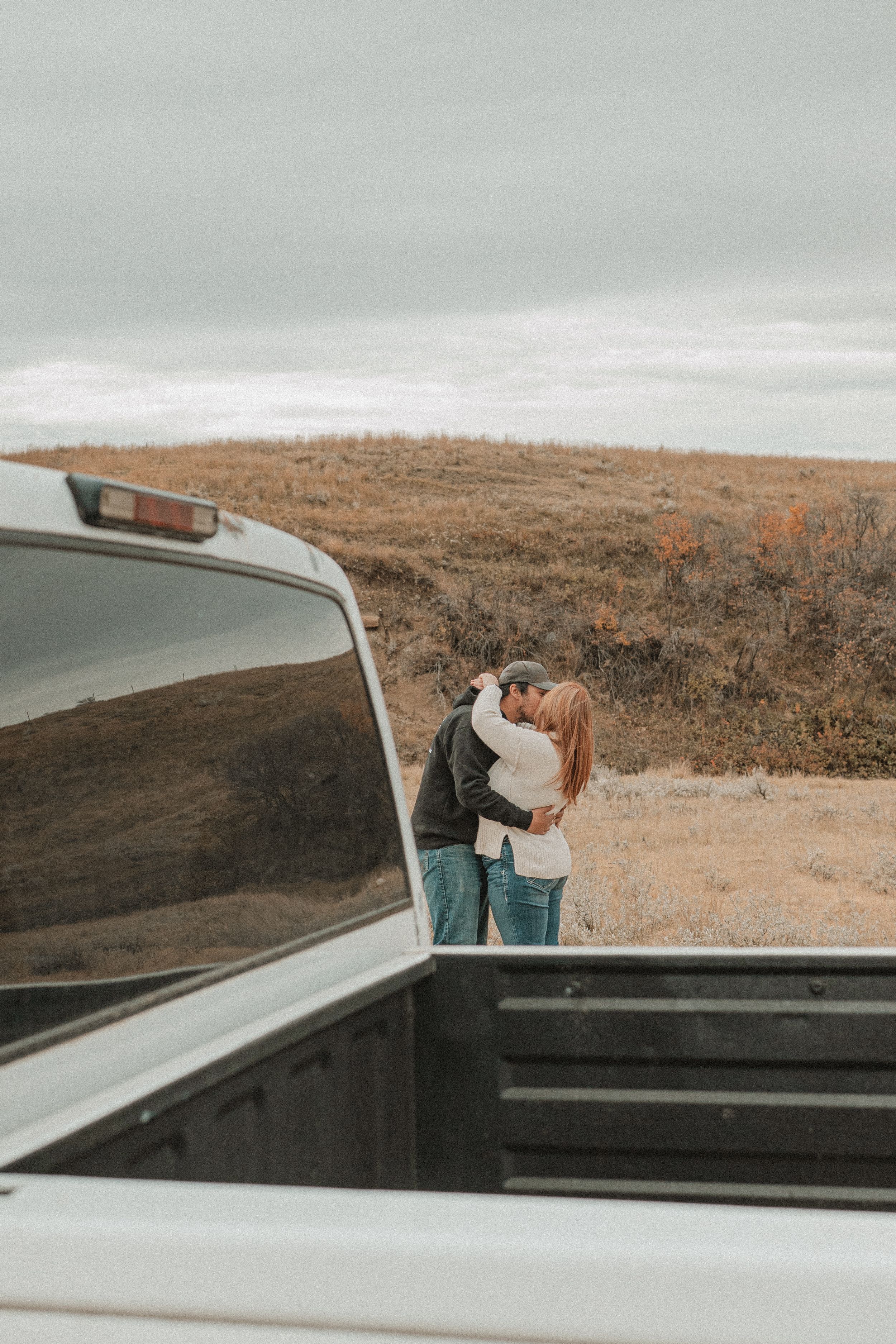 Couple sitting together on a car rooftop overlooking a scenic coastal landscape on an overcast day.