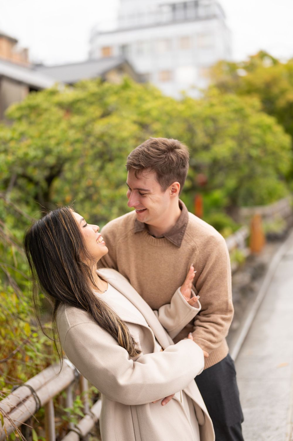 Couple embracing and gazing at each other lovingly near a lush green garden in Kyoto.