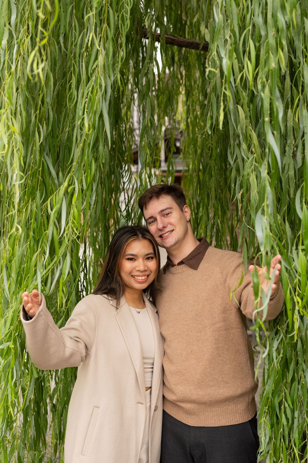 Smiling couple posing together under cascading green willow tree branches in Kyoto, Japan.