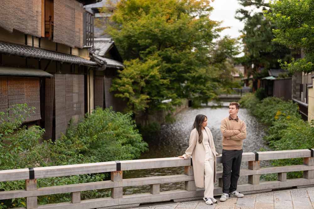Couple standing on a wooden bridge over a serene canal in Kyoto, Japan, surrounded by lush greenery.
