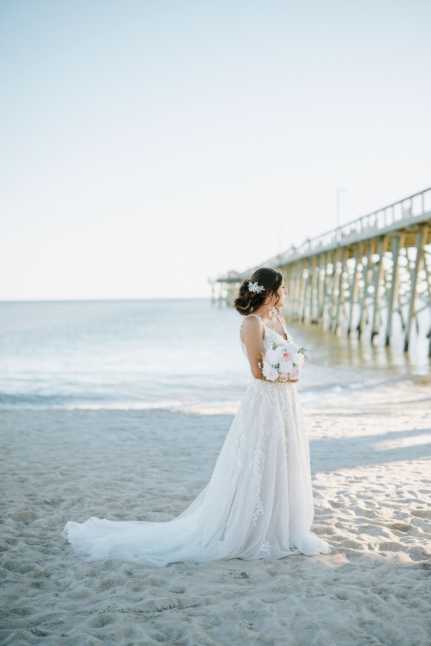 A romantic beach photoshoot with a white gown against a pier backdrop during golden hour.