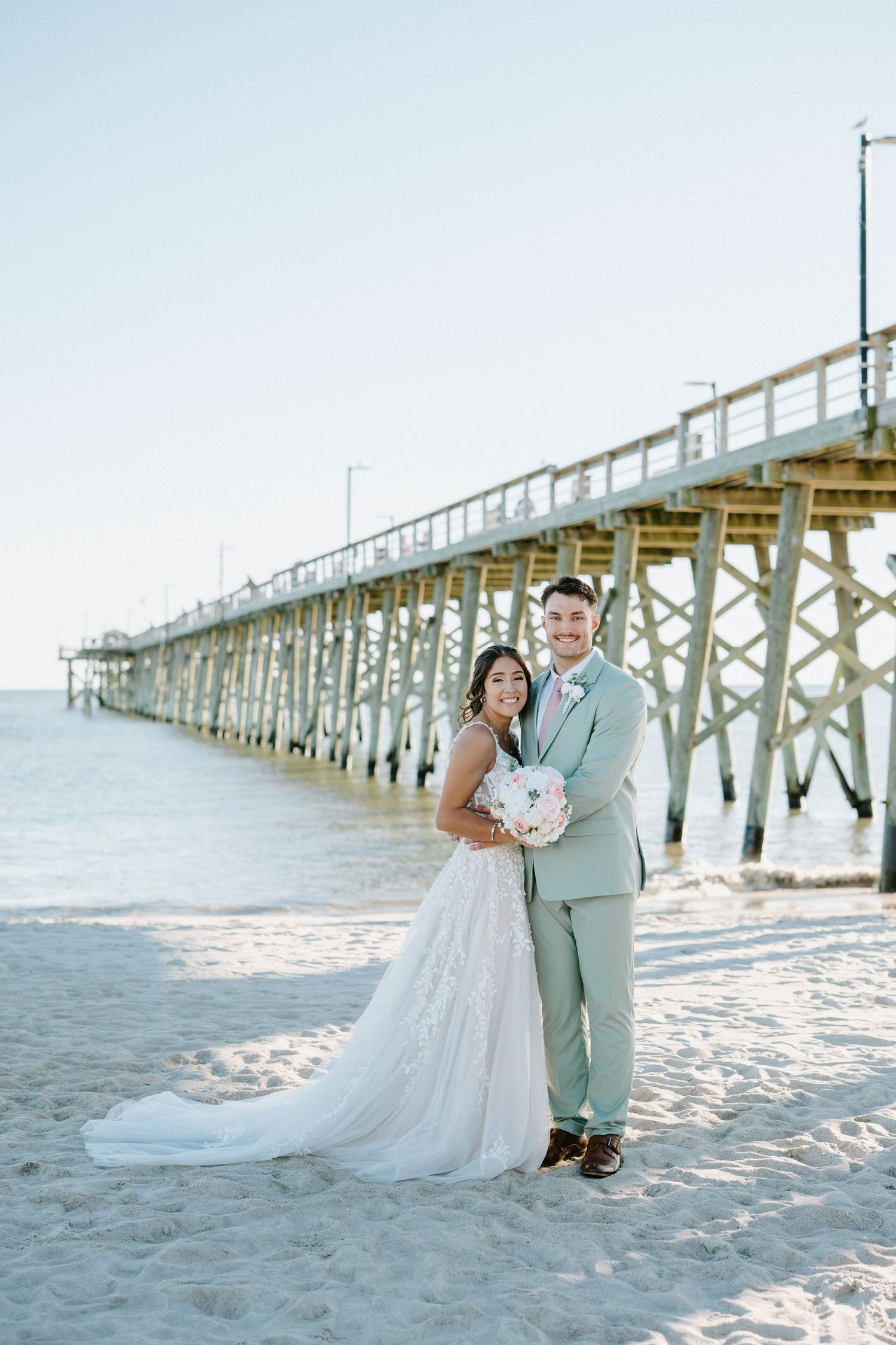 A romantic beach wedding photo session with a wooden pier backdrop during sunset.