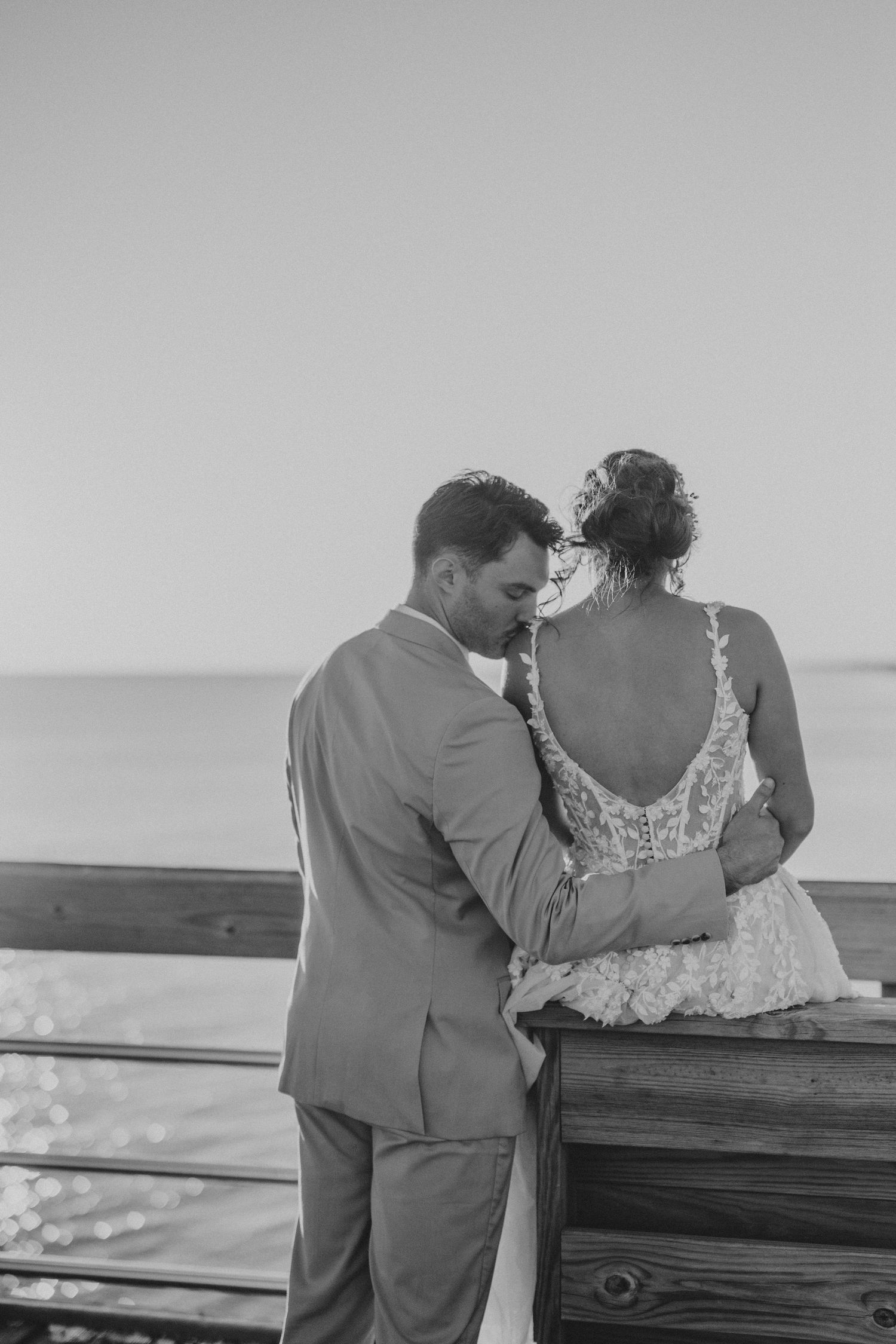 A romantic black and white photo series of a couple sharing an intimate moment on a wooden pier by the ocean.
