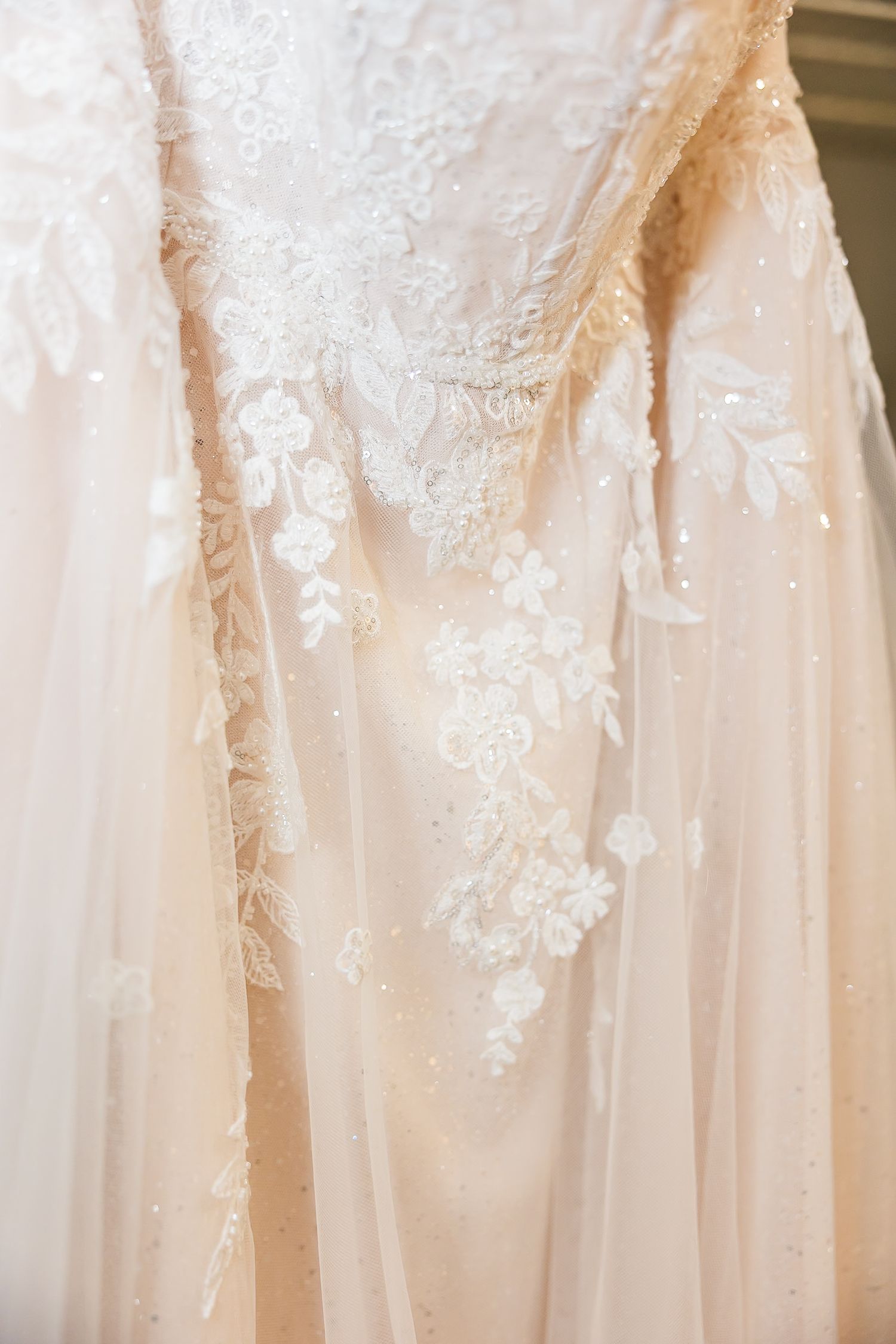 Long hotel hallway with beige carpeting and white wedding dresses hanging on doors creates an elegant atmosphere.