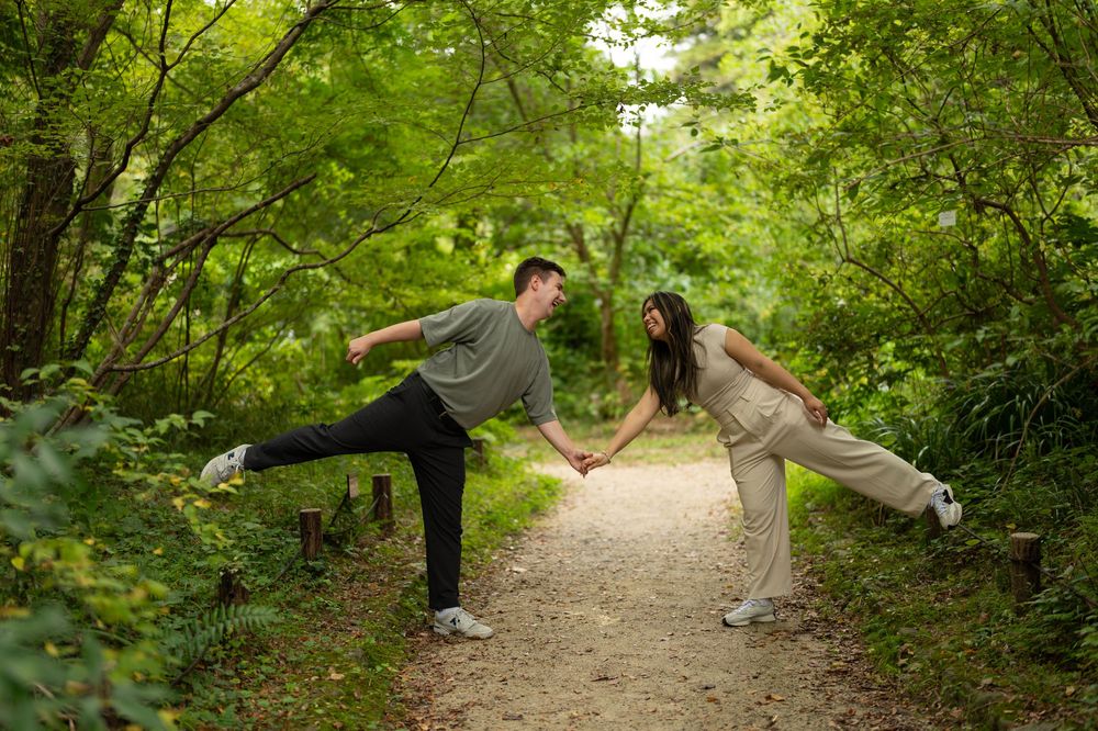 Playful couple leaning toward each other while holding hands on a forest path.