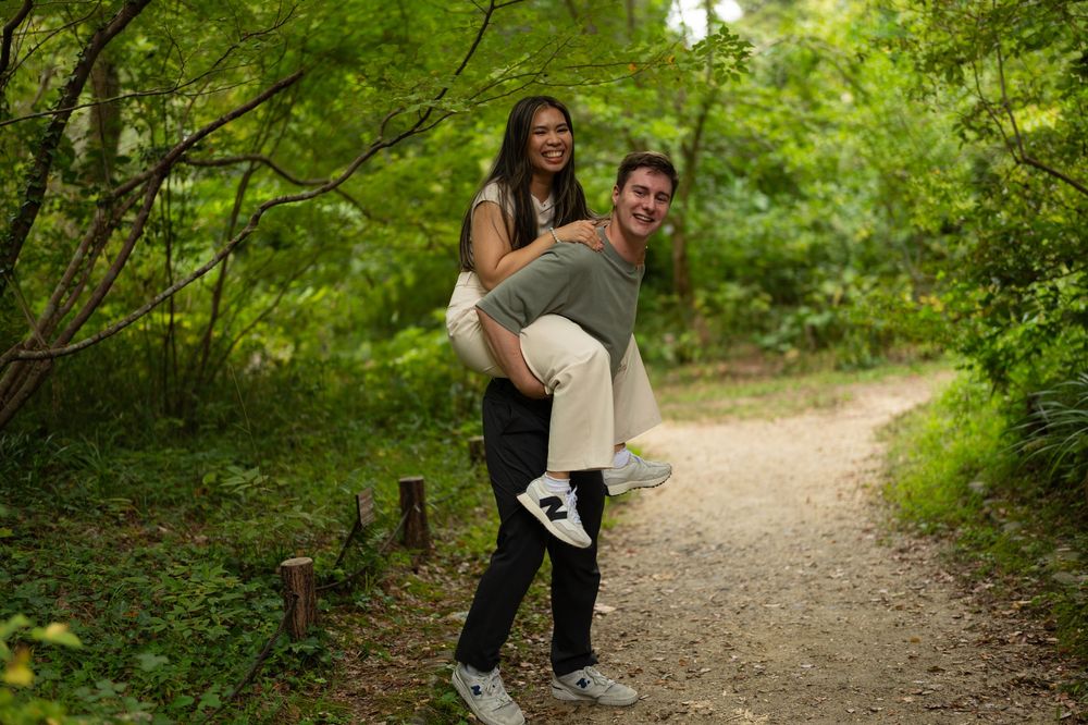 Man giving woman a piggyback ride on a scenic forest path while smiling.