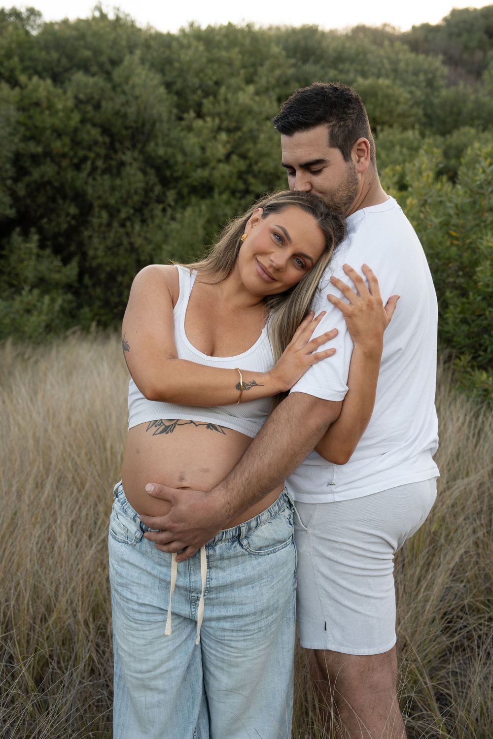 Expecting parents sharing a tender moment in long grass during their Wollongong maternity session.