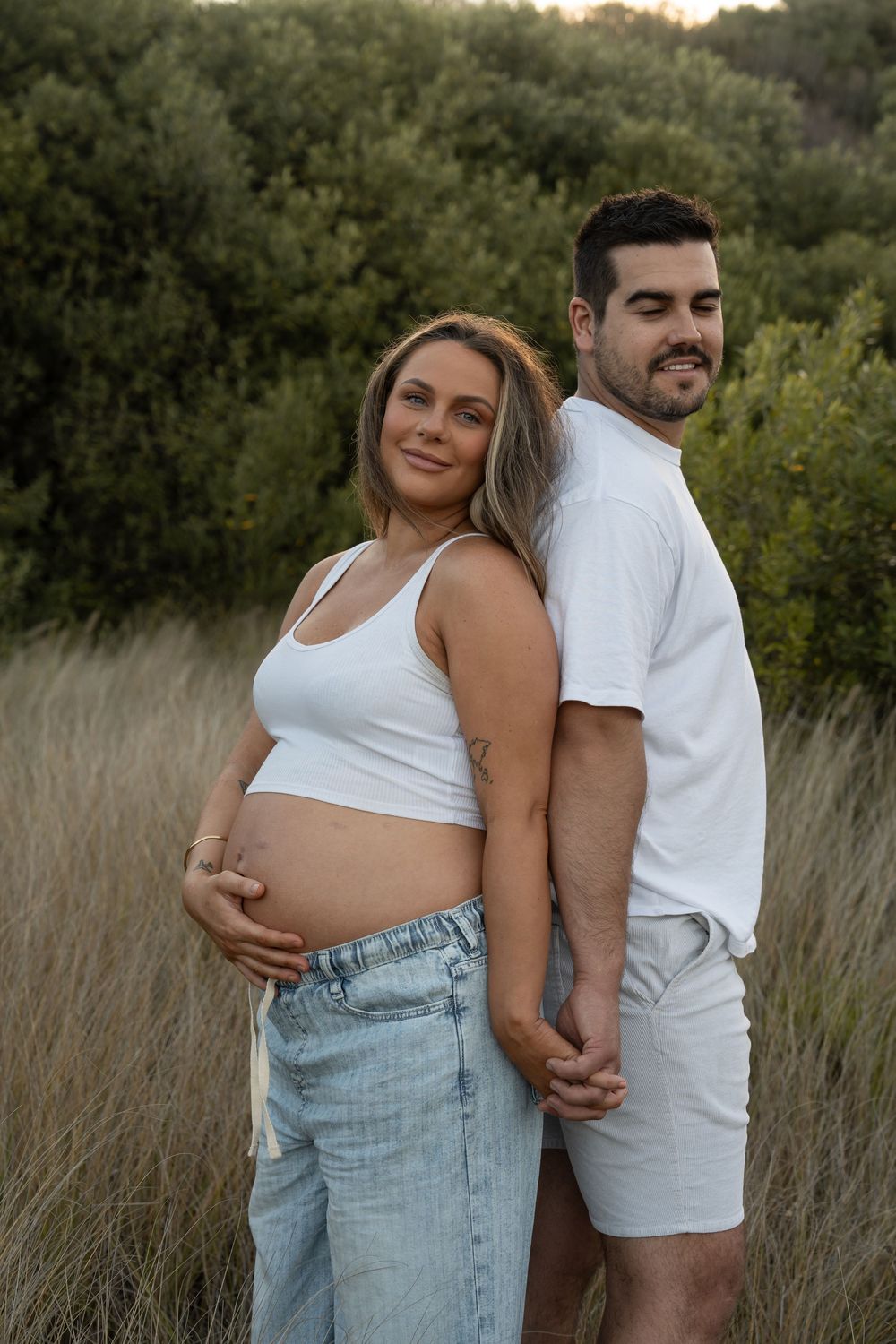 First-time parents embracing in long grass during their natural maternity photography session in Wollongong