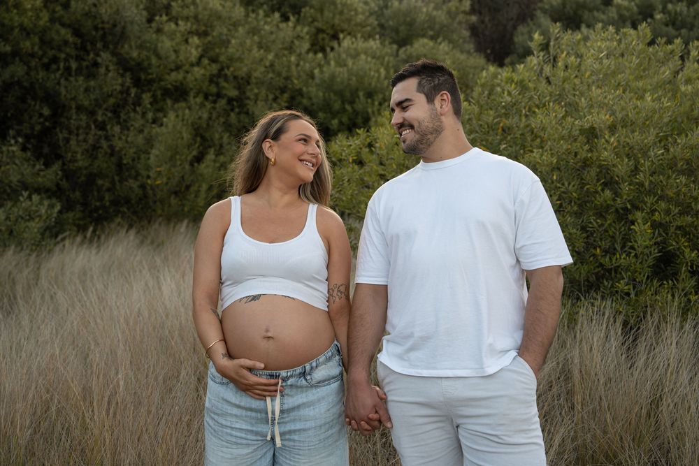 Candid maternity portrait in long grass capturing love, connection, and anticipation in Wollongong