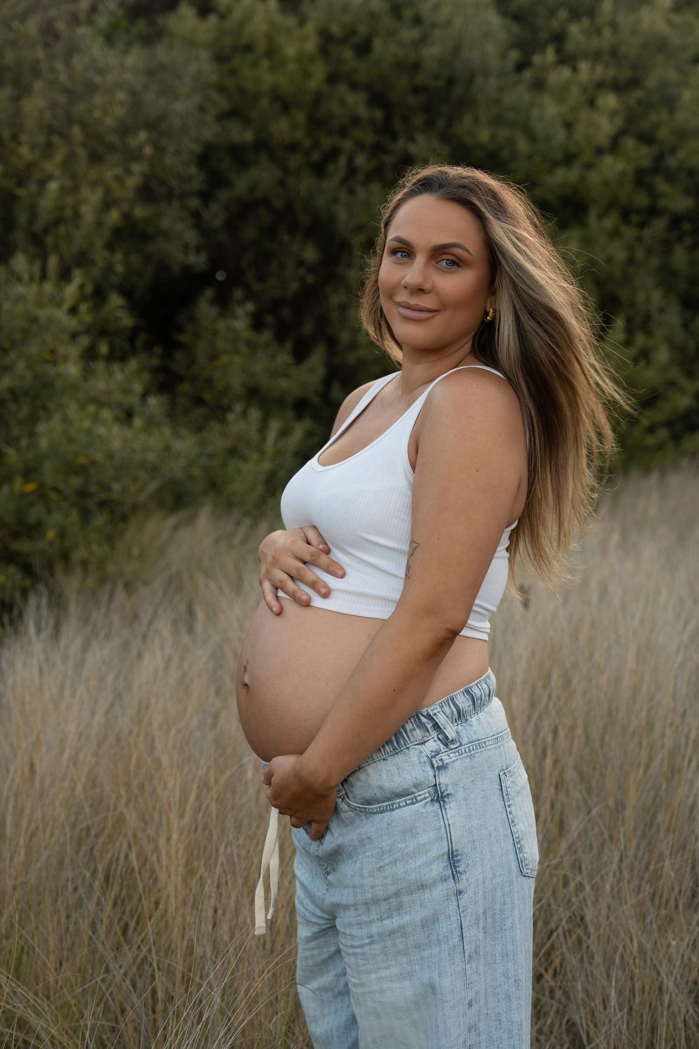 Beautiful first-time mum surrounded by long grass during maternity photoshoot in Wollongong
