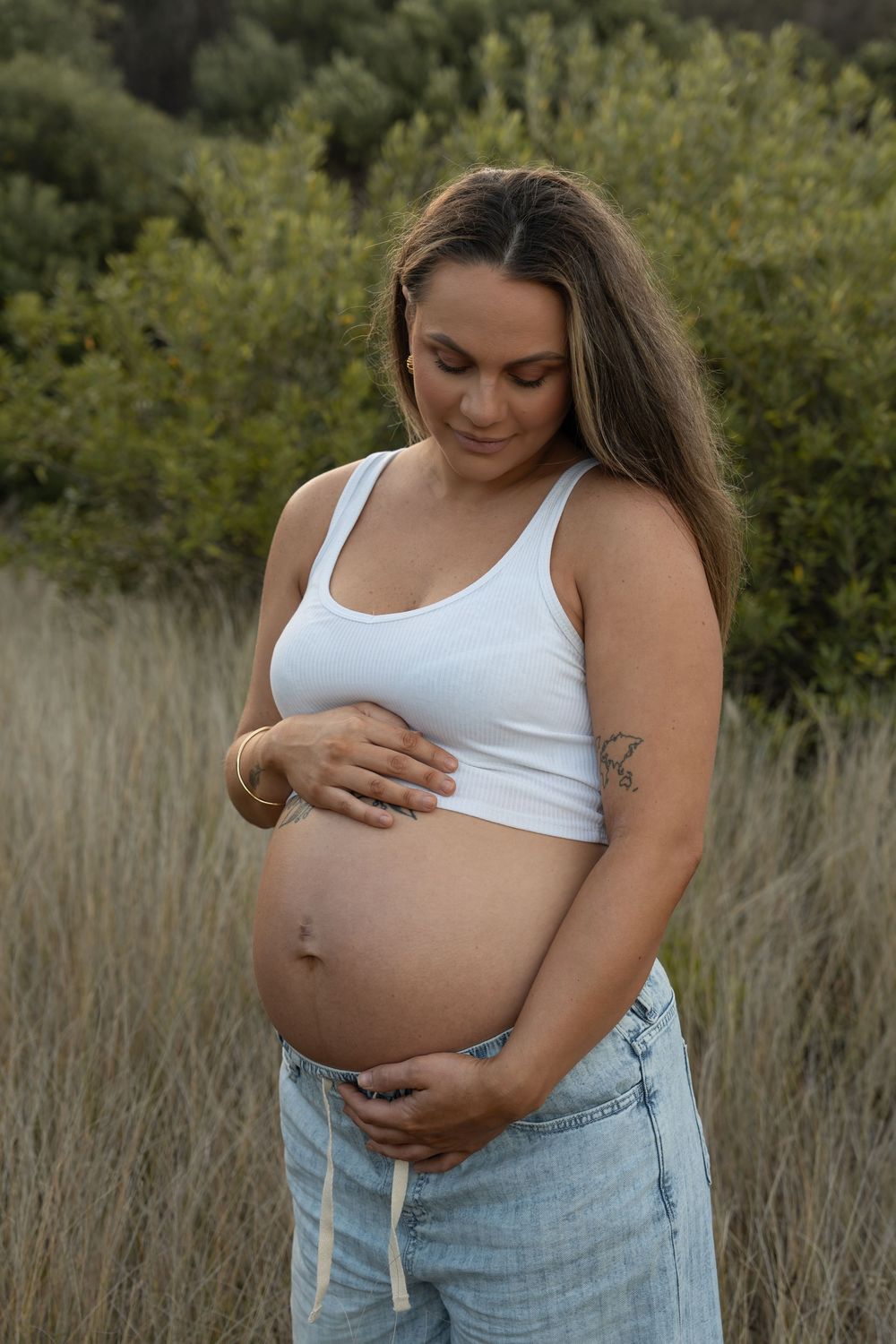 Expecting mum holding her baby bump in soft sunset light among long grass in Wollongong