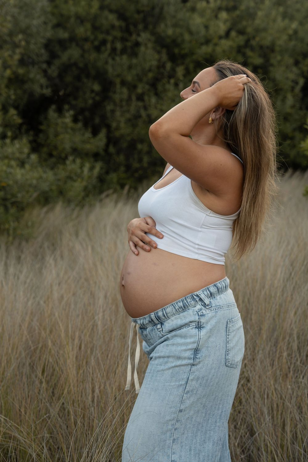 Expecting mum holding her baby bump in soft sunset light among long grass in Wollongong