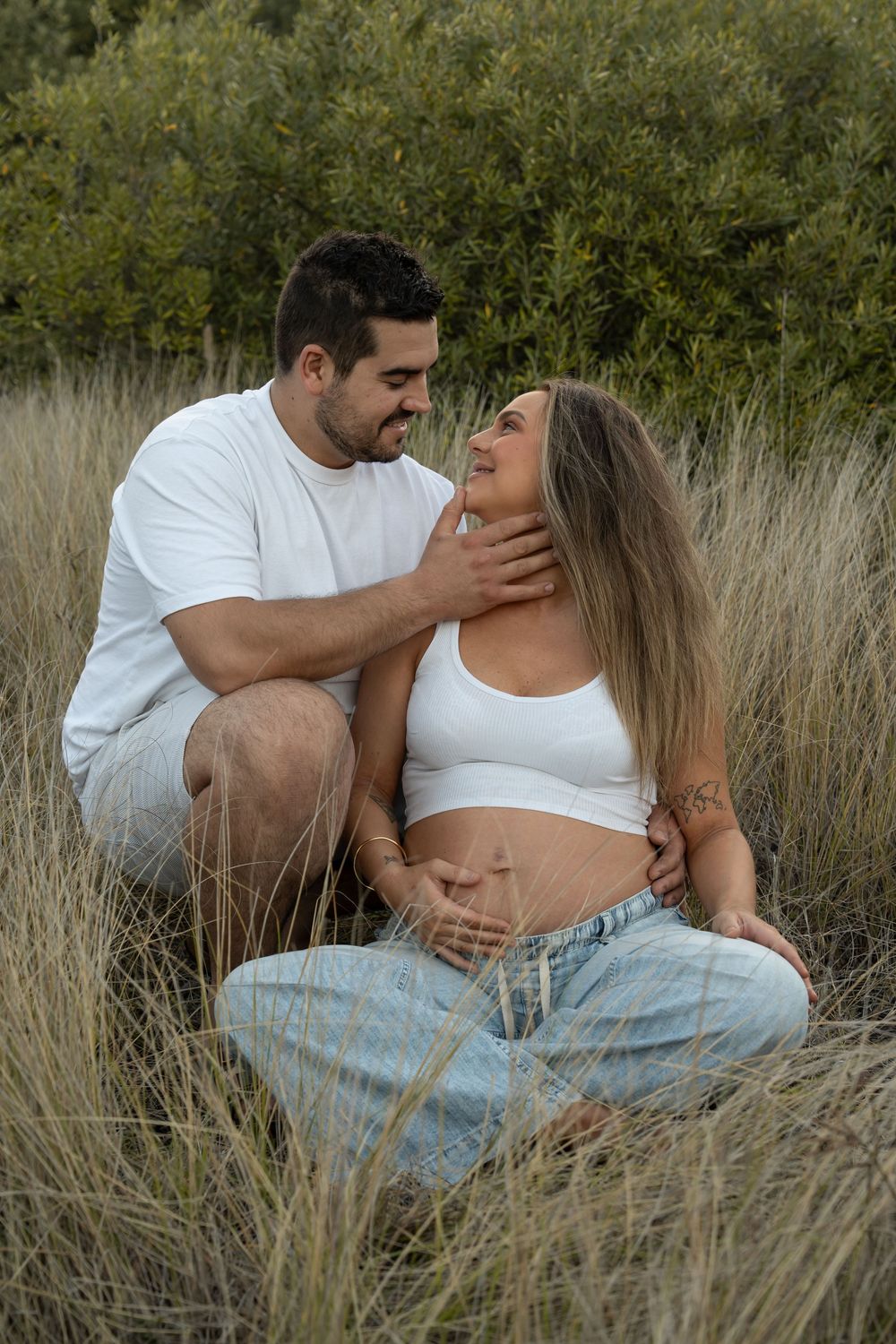 Expecting parents embracing in long grass during maternity photoshoot in Wollongong