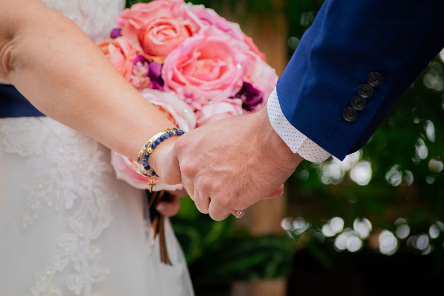 Close-up of pink rose bouquet and hands during wedding ceremony.