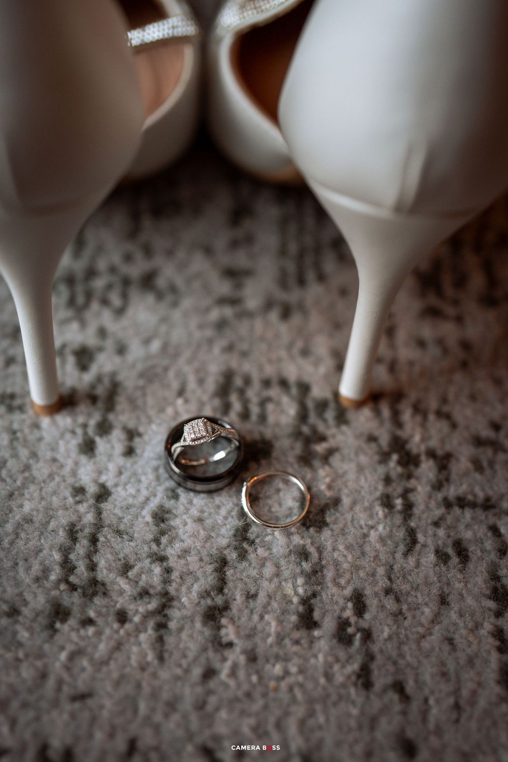 Wedding rings photographed on a textured stone surface with ceramic figurines in the background.